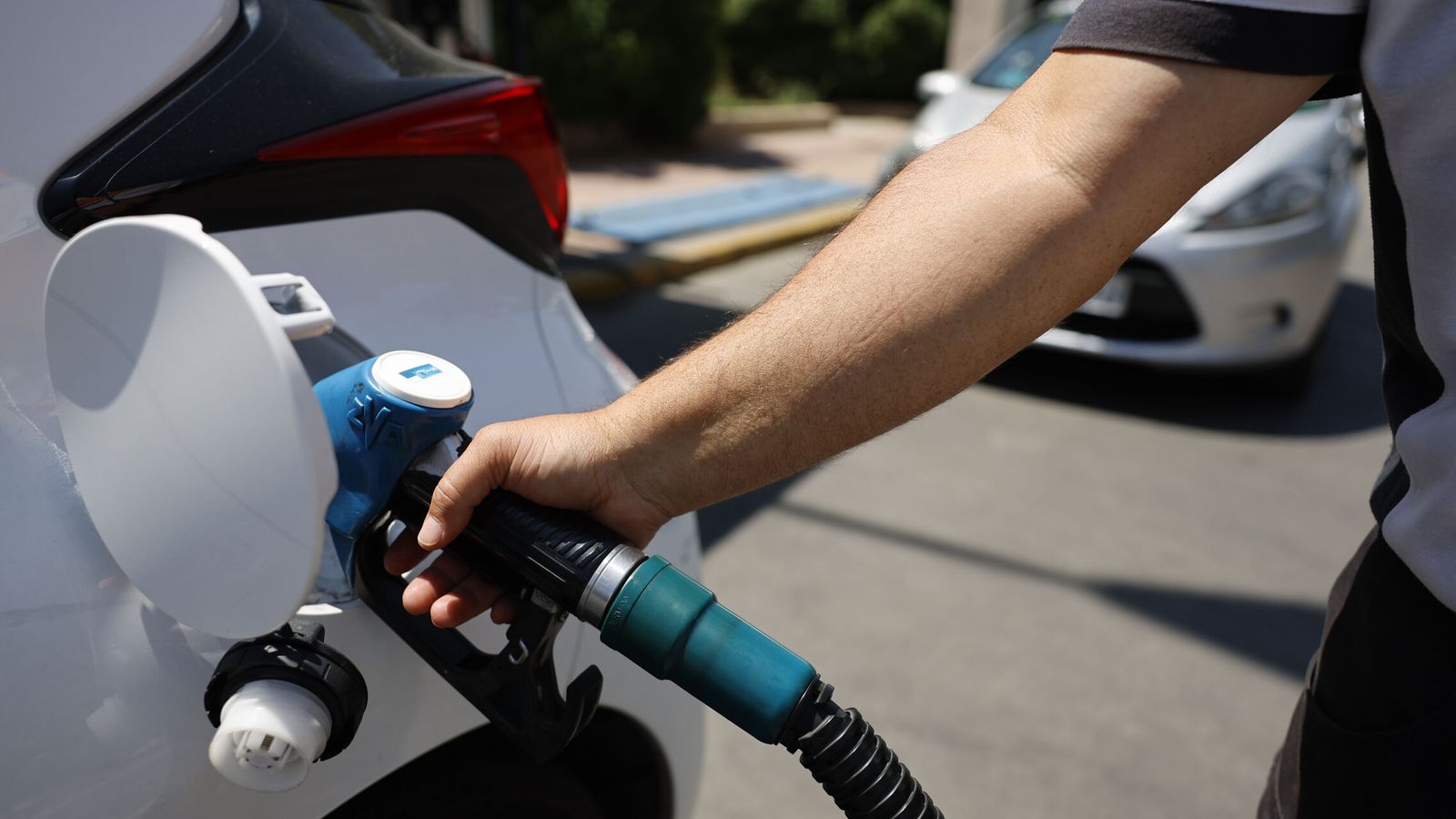 Conductores en una estación de servicio con carteles de descuento en carburantes